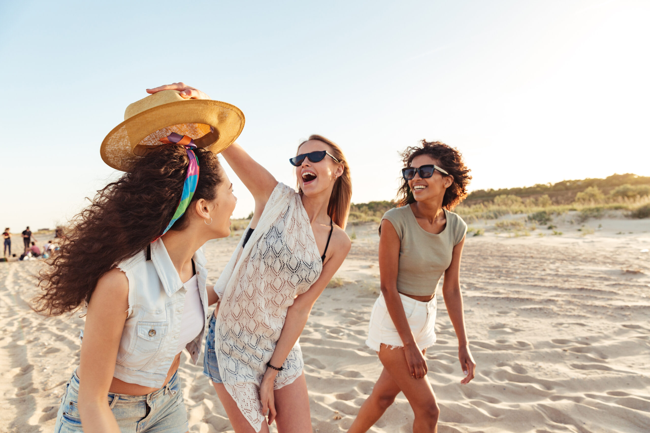 Three excited girls friends in summer clothes talking while walking together at the beach